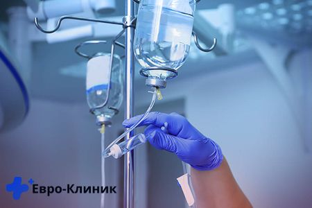 Рука врача в перчатке поправляет пакет капельницы